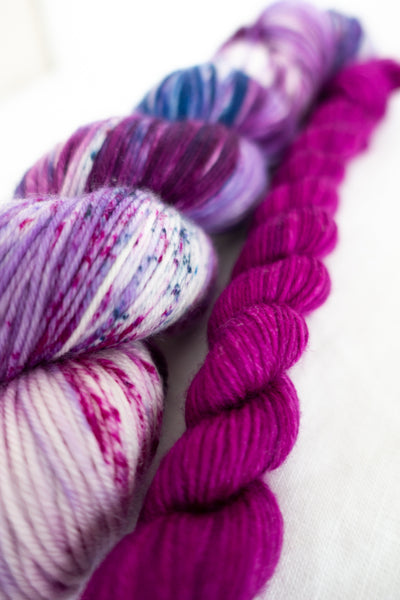 Skip Rope Yarn Co sock set - one full size skein of yarn in purple, blue and pink with a 20 gram mini-skein in pink on a white background
