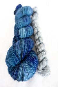Skip Rope Yarn Co sock set - one full size skein of yarn in a blue shade with a 20 gram mini-skein in light grey on a white background