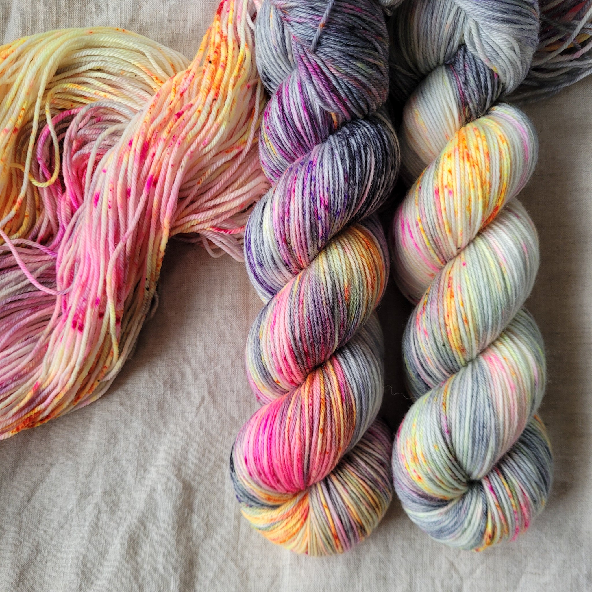 Skeins of hand dyed yarn with pink and orange speckles on a grey base