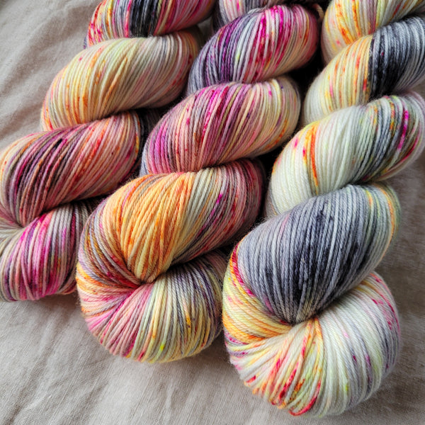 Skeins of hand dyed yarn with pink and orange speckles on a grey base